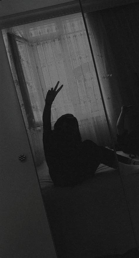 Black And White Photograph Of Woman Sitting On Bed In Dark Room With Large Glass Door