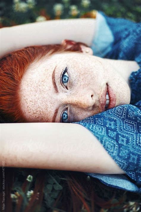 A Woman With Freckled Hair And Blue Eyes Is Laying On Her Back In The Grass