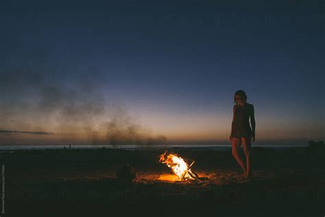 Woman Enjoying The Warmth Of A Bonfire On The Beach Under The Stars