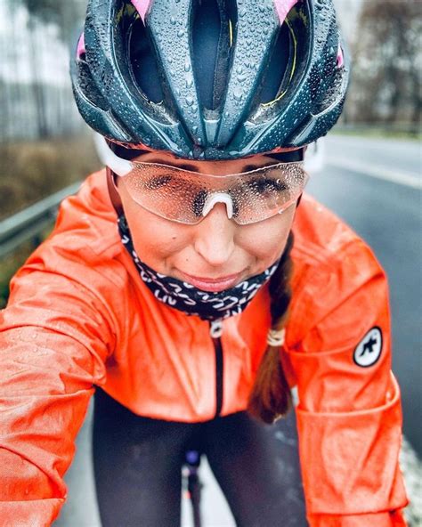 A Woman In An Orange Jacket Is Riding Her Bike Down The Street With Goggles On