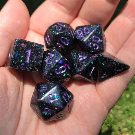 Five Black Dice With Purple And Green Holographics On Them In The Palm Of Someones Hand
