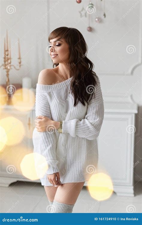 Beautiful Brunette Model Girl In A White Sweater Poses Against The Background Of The Christmas