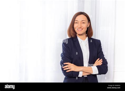 Portrait Of Beautiful Businesswoman In Blue Suit Jacket Standing With Arms Folded Against White