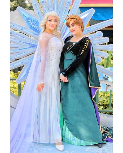 Two Women Dressed As Disney Characters Pose For A Photo In Front Of A