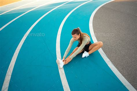 Female Runner Doing Stretching Exercises Sitting On Running Track Stock