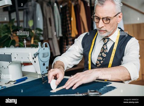 Senior Tailor Making Pattern On Cloth With Piece Of Chalk At Sewing