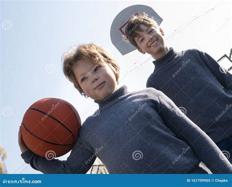 Two Happy Young Boys Playing Basketball Outdoors On A Sports Field