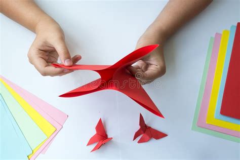 Children`s Hands Do Origami Butterfly From Colored Paper On White