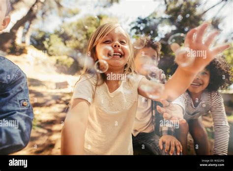 Group Of Children Playing With Soap Bubbles In Forest Girl With