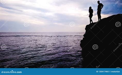 Loving Couple Standing On Edge Of Rock Preparing For Jump Into Water