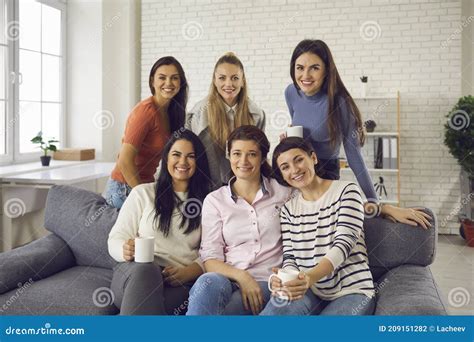 Group Of Happy Young Women Sitting On Couch Enjoying Tea Smiling And Looking At Camera Stock