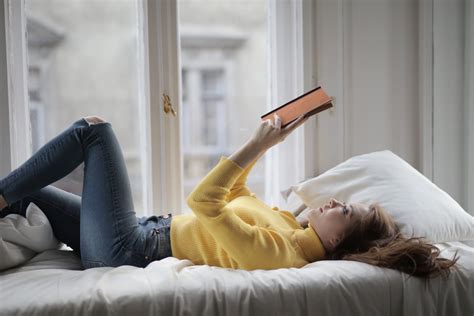 Woman In Yellow Sweater Lying On Bed While Reading Book · Free Stock Photo