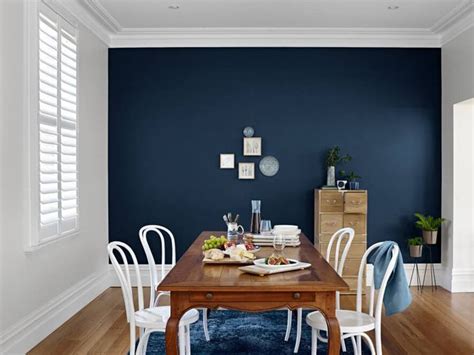 A Dining Room With Dark Blue Walls And White Chairs Around A Wooden
