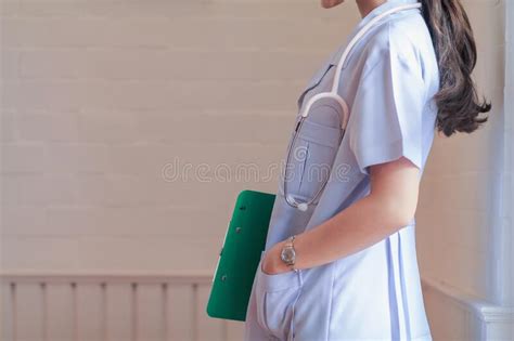 A Uniformed Female Doctor Stands By A Window In Her Office Holding A Clipboard Showing The