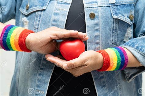moça asiática usando pulseiras arco íris e segurando o símbolo vermelho do coração do mês do