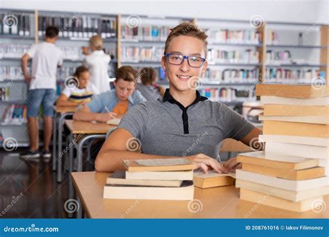 Schoolboy Sitting With Stacks Of Books In School Library Stock Photo