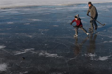 Man And Boy Playing Hockey On Frozen Pond Ice In Winter Del