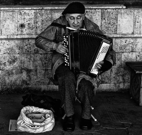 An Old Man Sitting On The Ground Playing An Accordion