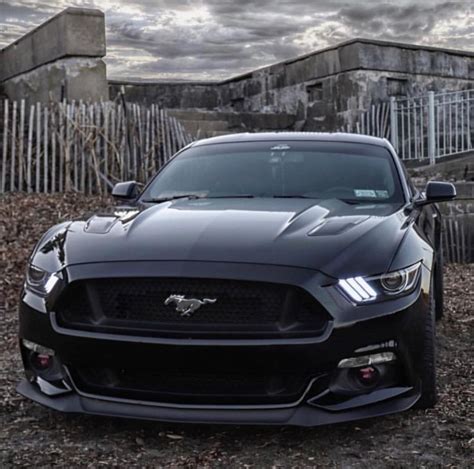 The Front End Of A Black Mustang Parked On Top Of A Dirt Field With