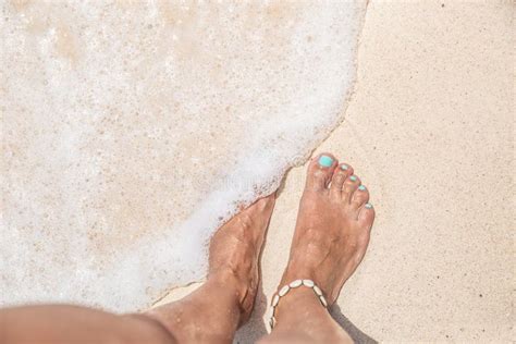 Bare Feet Of A Woman With Turquoise Nail Polish Standing On A Sandy