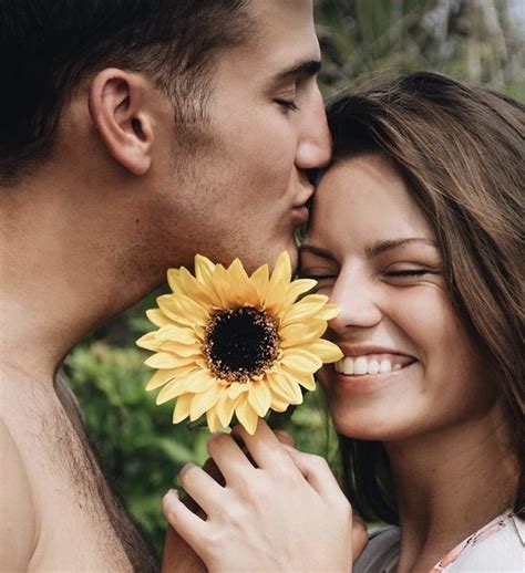 A Man Kissing A Woman S Forehead With A Sunflower In Front Of Her