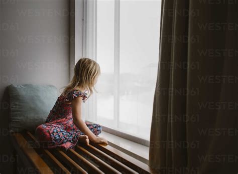 Side View Of Girl Looking Through Window While Sitting At Home Stock Photo