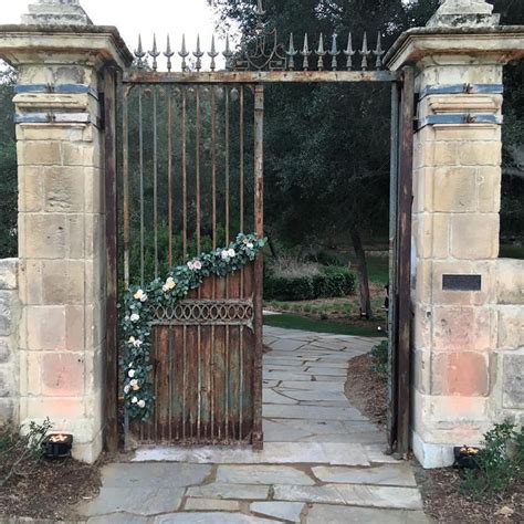 An Iron Gate With Flowers On It And Stone Walkway Leading To The