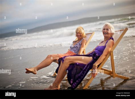 Two Happy Mature Women Relaxing In Deck Chairs On The Beach Stock Photo