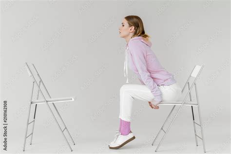 Side View Of Stylish Young Woman Sitting On Chair In Front Of Another