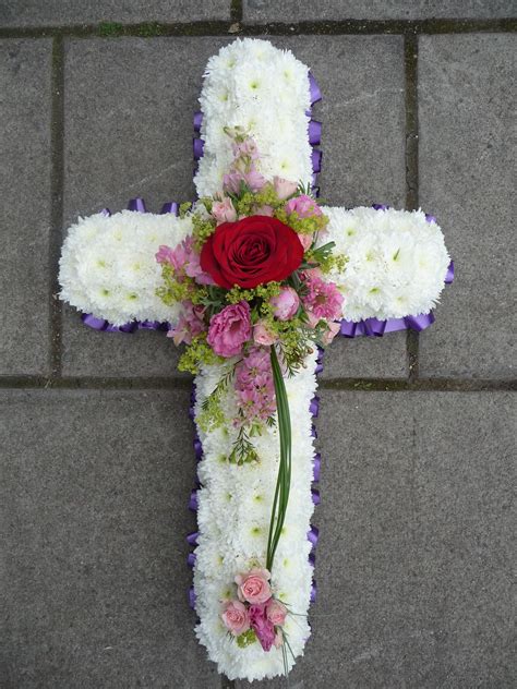 A Small White Based Funeral Cross With A Red Rose Pink Flower Sprays