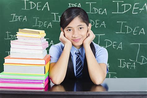 High School Girl Student Sitting At Desk Leaning On Stack Of Books In