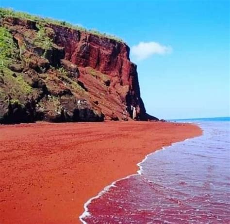Red Sand Beach With Cliffs On The Side And Water In The Foreground