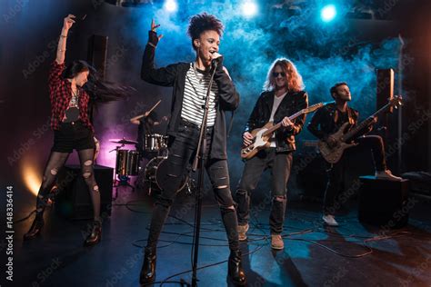 female singer with microphone and rock and roll band performing hard rock music on stage stock