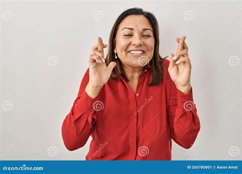 Hispanic Mature Woman Standing Over White Background Gesturing Finger Crossed Smiling With Hope