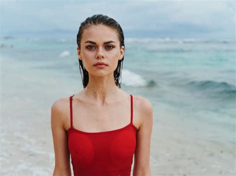 beautiful woman in a red swimsuit looks at the camera on the ocean beach with wet hair stock