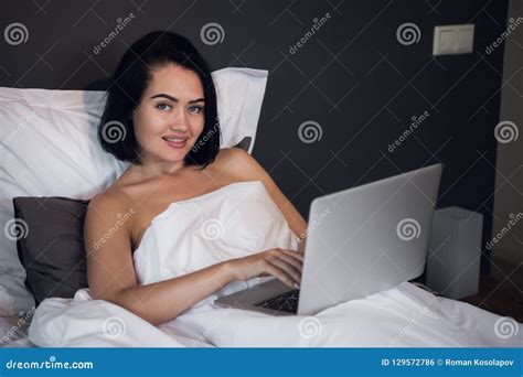 Woman Working On Laptop Computer While Lying On A Bed At Home Stock