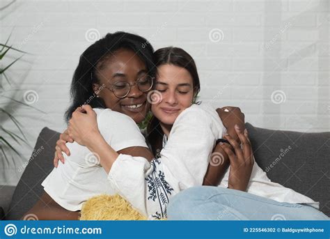 Jovem Lindíssima Casal Lésbica Negra Africana E Caucasiana Sentada No Sofá Em Sua Casa Abraçando