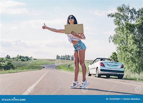el autostopista sonriente de la mujer en el camino está llevando a cabo a un tablero en blanco