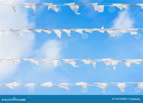 White Flags Of Triangular Shape Pennants Against Blue Cloudy Sky In