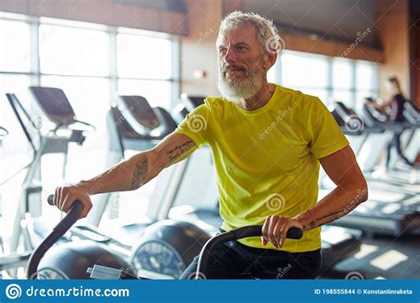 Staying Fit Focused Mature Athletic Man In Sportswear Doing Cycling On Exercise Bikes At Gym