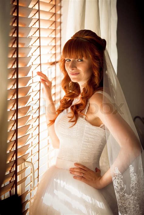 portrait of beautiful redhead bride posing at window with jalousie stock image colourbox