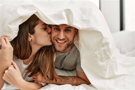 Young Caucasian Couple Covering With Bed Sheet And Kissing On The Bed