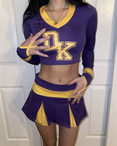 A Woman In A Purple And Yellow Cheerleader Outfit Posing For The Camera With Her Hand On Her Hip