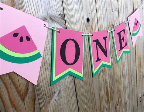 One In A Melon Banner Hanging On A Wooden Fence With Watermelon Slices