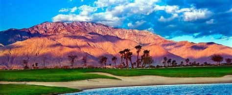A Golf Course With Palm Trees And Mountains In The Background At Sunset