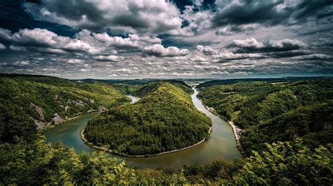 Aerial View Of River Between Green Trees Covered Forest Under Cloudy