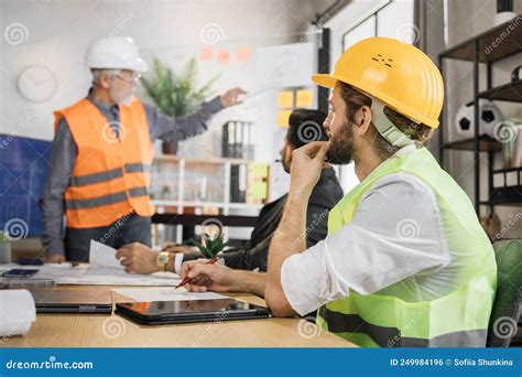 Attractive Man In Reflective Vest Sitting At Table With Males