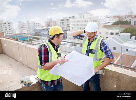 Construction Worker And Engineer Reviewing Blueprints At Highrise