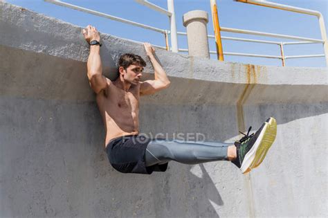 Young Man Doing Sit Ups Outdoors Hanging On A Wall Without A Shirt