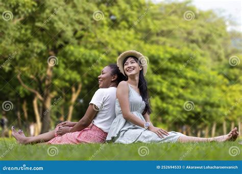 diversity of lgbtq lesbian couple is relaxingly sitting together on the grass lawn in public